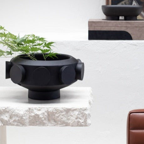 A resin large pedestal bowl with black cylinders on the exterior or perimeter